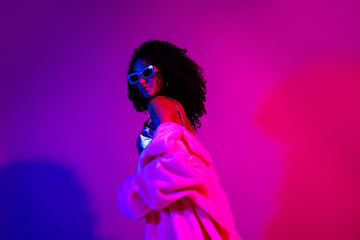 Stylish female model glowing under vivid neon lights in a modern retro-inspired setting with vibrant purple and pink hues.