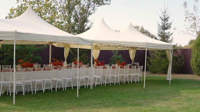 Orange autumn flowers dahlias on table with decor, floristry and food. Outdoor tent in nature. Festive buffet and many delicious dishes with glasses at banquet and celebration of wedding and event