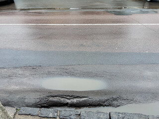 Damaged asphalt road with a large puddle and pothole after rain. Common urban infrastructure issue, representing poor road maintenance and weather impact. High quality photo