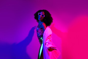 Glamorous young woman posing under vibrant neon lights in an energetic nightclub atmosphere