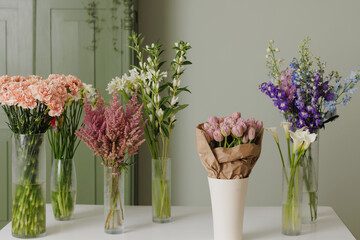 Elegant floral arrangement with fresh colorful flowers in glass vases on a white table against a soft green background, creating a serene atmosphere, flowers in vases in a flower shop