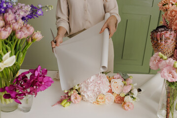 Florist wrapping a fresh bouquet in elegant paper, preparing a stylish floral arrangement for...