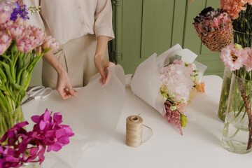Florist wrapping a fresh bouquet in elegant paper, preparing a stylish floral arrangement for gifting or sale. flower shop
