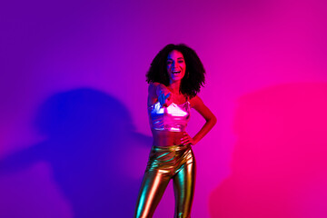 Young woman in vibrant neon lighting wearing metallic stylish clothing, dancing joyfully while enjoying the party vibe