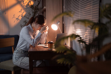 Young asian female entrepreneur is having headache and feeling tired while working late at night in her home office, burnout and overtime working concept