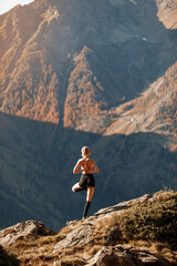 Fototapeta premium A young slender girl does yoga against the backdrop of beautiful nature among the mountains. Healthy lifestyle concept