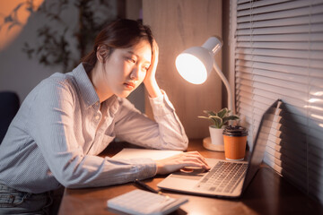 Young stressed businesswoman having headache and massaging her head while working with laptop computer at night in office, feeling tired and overworked