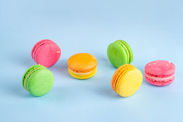 Bright and colorful sweet macaroons dessert with fresh berries. Pink, orange, yellow and pistachio green tasty macaron cookies on light blue background copy space