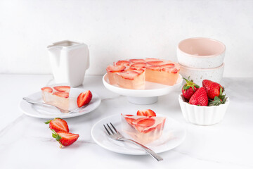 Japanese Raindrop Cake, or Mizu Shingen Mochi, clear jelly dessert, crystal-clear water-like delicacy agar pudding tart with strawberry slices, portioned on plates, white marble background copy space