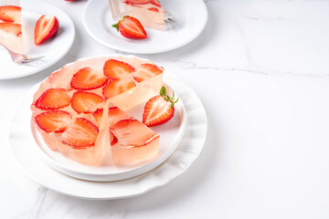 Japanese Raindrop Cake, or Mizu Shingen Mochi, clear jelly dessert, crystal-clear water-like delicacy agar pudding tart with strawberry slices, portioned on plates, white marble background copy space