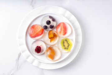 Japanese Raindrop Cake, or Mizu Shingen Mochi, clear jelly dessert, crystal-clear water-like delicacy agar pudding with fruit and berry slices, portioned on plates, white marble background copy space