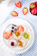 Japanese Raindrop Cake, or Mizu Shingen Mochi, clear jelly dessert, crystal-clear water-like delicacy agar pudding with fruit and berry slices, portioned on plates, white marble background copy space