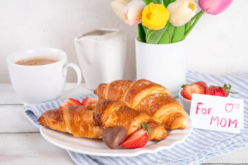 Mother’s Day breakfast background featuring croissant, strawberries, chocolates, coffee mug, bouquet of tulip flowers, as surprise and gift, with greeting card 