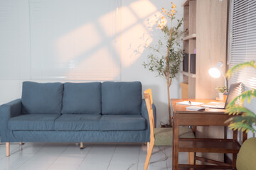 Comfortable home office interior design with a laptop, desk lamp, wooden desk and chair, a blue...