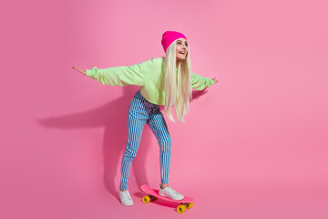Young stylish woman balancing playfully on a skateboard against a vibrant pink backdrop, wearing trendy and colorful fashions