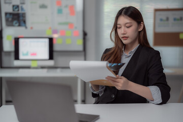 Young businesswoman sitting at her desk, intently reviewing financial documents while showcasing her focus, professionalism, and expertise in the corporate environment
