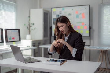 Obraz premium Young professional woman feeling a wrist pain while working on laptop computer in modern office, suffering from carpal tunnel syndrome after long hours of using computer mouse and keyboard