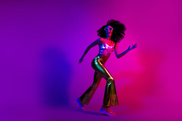 Energetic young female dancing in retro-inspired neon lighting wearing metallic fashion for a vibrant and colorful photoshoot