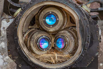 Close-up of metallic equipment with three angled lenses, likely a camera or optical sensor Textured exterior, one lens has a blue interior No context provided about its purpose or origin