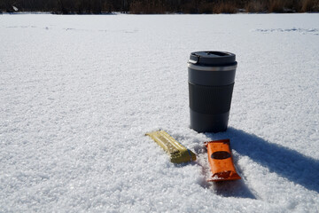Thermos mug with hot drink and food bars in the snow
