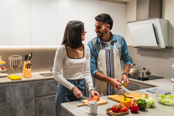 Happy couple preparing dinner, cutting vegetables in modern kitchen