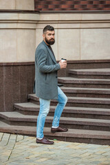 Obraz premium Business lifestyle, break. Man drinking morning coffee. Coffee break. Everyday style routine. Bearded man having coffee in city street. Handsome man on street holding cup of drink. Coffee to go