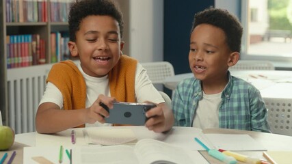Cute funny little boys African American kids siblings brothers happy children school pupils schoolboys students friends playing mobile phone online video game together addicted gaming play smartphone - Powered by Adobe