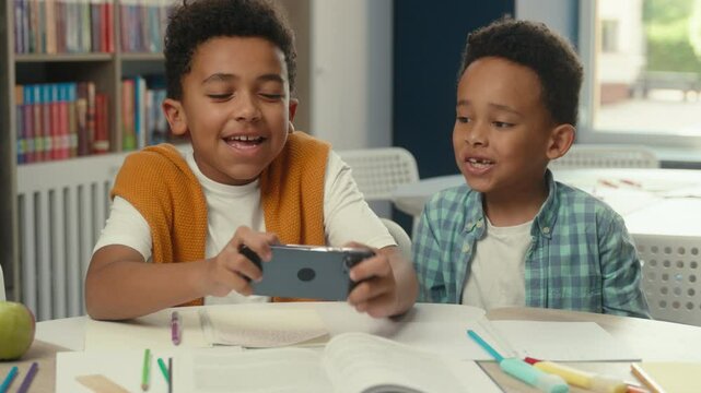 Cute funny little boys African American kids siblings brothers happy children school pupils schoolboys students friends playing mobile phone online video game together addicted gaming play smartphone