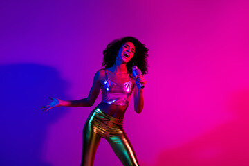 Young woman singing with a microphone in a vibrant neon-lit room, expressing joy and energy...