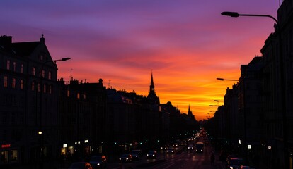 Fototapeta premium City street at sunset with striking orange and purple sky above buildings.