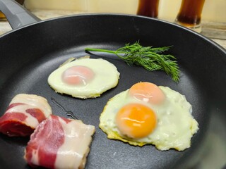 An overhead view of a frying pan breakfast of fried eggs and delicious bacon. Glasses of beer are in the background