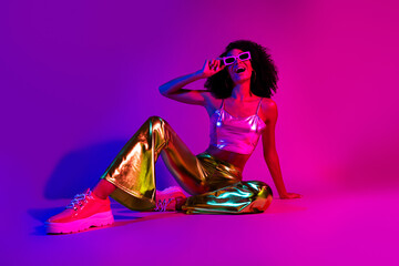 Glamorous young woman posing in vibrant neon lights, showing stylish metallic fashion and joyful energy, evoking retro nightlife vibes.
