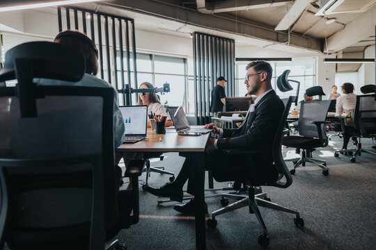 A team of business people engaged in a meeting within a contemporary open plan office. Business employees are using laptops for collaboration, emphasizing modern workplace environments and teamwork.