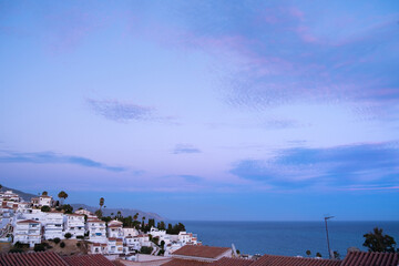 View of a coastal town of Andalusia in southern Spain. It is driving and the sky has pink and blue tones. The houses are typical of the area and the sea is calm © LaMorenita