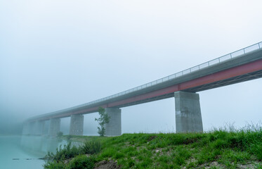Fototapeta premium Bridge over Sylvenstein lake on a foggy morning, side view from under the bridge