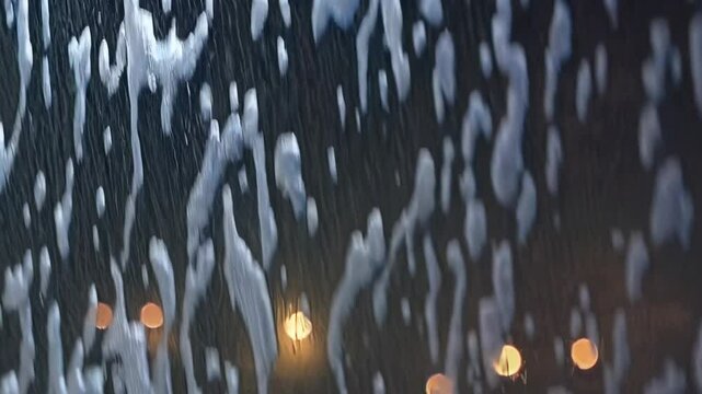 Raindrops and city lights: softly blurred urban nightscape with falling water