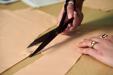 Dressmaker cutting dress fabric on sketch line with sewing machine. Fashion designer tailor or sewer in workshop studio designing new collection clothes. Business owner