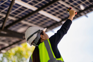 A female technician in a hard hat and reflective vest conducts a solar panel inspection with a...