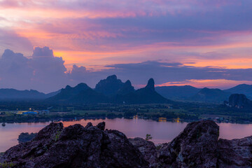 Phusab Lek : LOPBURI, THAILAND, Serene Twilight over Mountains and Water: An evocative landscape painting of mountains reflecting in tranquil water under a colorful twilight sky, with soft hues of pin