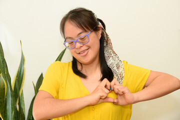 Portrait of a girl with Down syndrome laughing while making a heart shape with her hands. Trisomy...