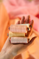 Hand holding Raw White Polyester FDY Yarn spool, Polyester Filament Yarn spool.PET fiber Yarn,spun polyester sewing thread with peach background.