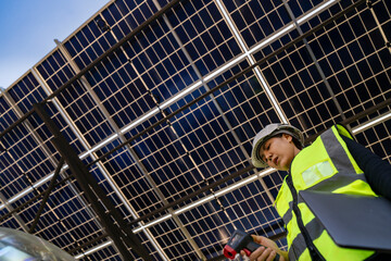 Technician inspects solar panels under a large solar carport structure. Focused on clean energy,...