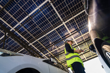 Technician inspects solar panels under a large solar carport structure. Focused on clean energy,...
