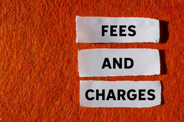 Fees and charges message written on ripped torn white paper pieces on orange background. Conceptual...