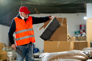 An older worker in a pet food warehouse prepares deliveries of goods for pet stores.