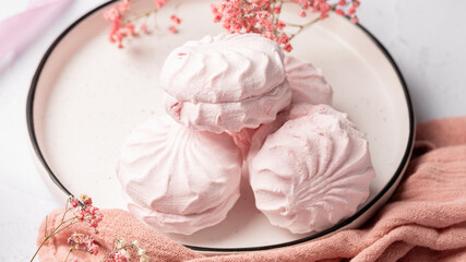 Pink berry marshmallow zephyr on white plate on a light background next to pink ribbons and flowers. White and pink zefyr made from applesauce and egg white. Low-calorie sweets. Vegan marshmallow.	
