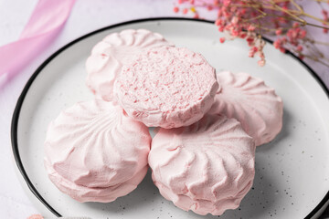 Pink berry marshmallow zephyr on white plate on a light background next to pink ribbons and flowers. White and pink zefyr made from applesauce and egg white. Low-calorie sweets. Vegan marshmallow.	