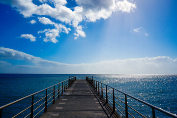 A striking ocean pier extends toward the horizon, offering a peaceful pathway into the vast, sunlit...