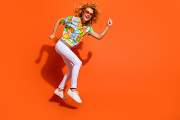 Portrait of a young woman jumping joyfully in colorful attire on an orange background, expressing happiness