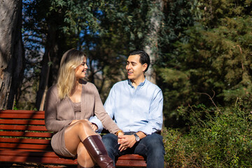 Fototapeta premium Latin couple holding hands and talking on park bench